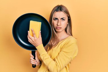 Güzel İspanyol kadın yemek pişirme tavasını temizlerken şüpheci ve gergin, sorun yüzünden somurtuyor. negatif kişi. 