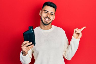 Sakallı, motor yağı şişesi tutan genç İspanyol adam gülümsüyor. 