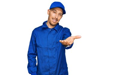 Sakallı, işçi tulumu giyen, neşeli gülümseyen, yardım eli uzatan ve kabul gören kel bir adam.. 