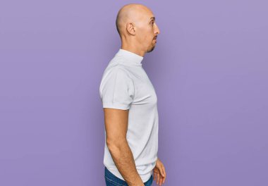 Sakallı, günlük beyaz tişörtlü, rahat bir görünüm takınan, kendine güvenen bir gülümsemesi olan kel bir adam.. 