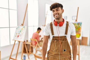 Sanat stüdyosundaki genç İspanyol adam yüzünde gülümseme ve doğal ifadeyle yan yana bakıyor. Kendinden emin gülen. 
