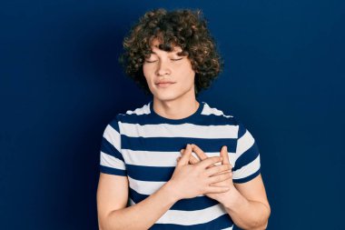 Yakışıklı, sıradan çizgili tişört giyen, elleri göğsünde, gözleri kapalı gülümseyen ve yüzünde minnet ifadesi olan bir genç. sağlık kavramı. 