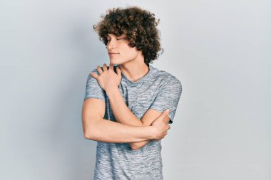 Yakışıklı, gri tişört giyen, kendine sarılan mutlu ve pozitif, kendinden emin gülümseyen bir genç. Sevgi ve özgüven. 