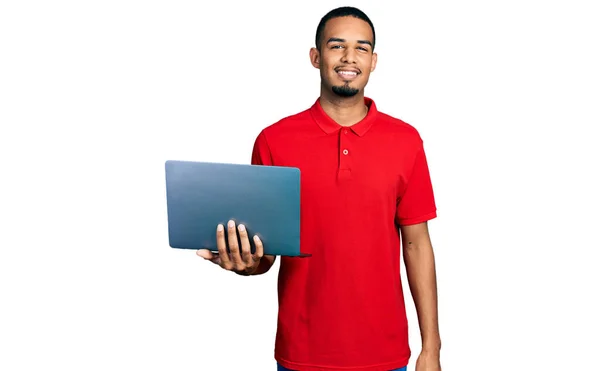 コンピュータのラップトップを使って仕事をしている若いアフリカ系アメリカ人の男性は 前向きな笑顔で立って笑顔で歯を見せています — ストック写真