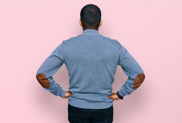 Young handsome hispanic man wearing casual sweatshirt standing backwards looking away with arms on body