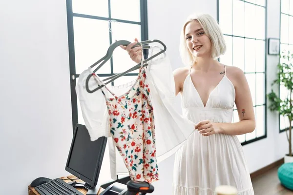 Giysi dükkanında kendine güvenen beyaz bir kadın gülümsüyor.