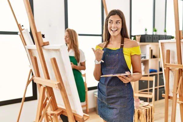 Young Hispanic Woman Art Classroom Pointing Thumb Side Smiling Happy — Fotografia de Stock
