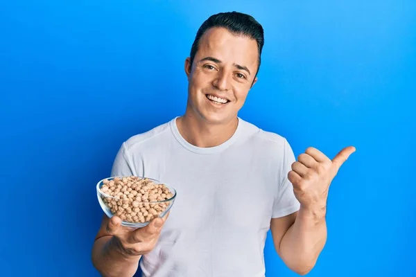 Handsome Young Man Holding Chickpeas Bowl Pointing Thumb Side Smiling — Fotografia de Stock