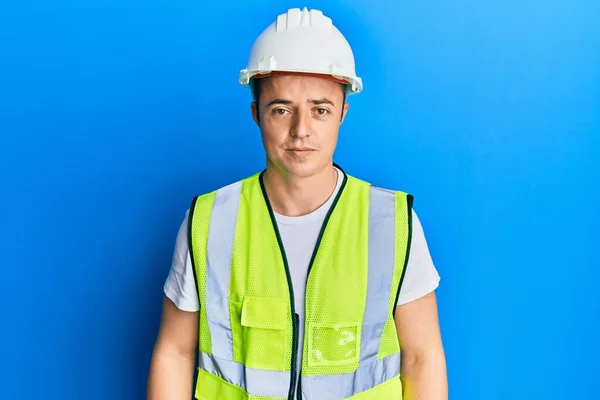 Handsome young man wearing safety helmet and reflective jacket with serious expression on face. simple and natural looking at the camera.