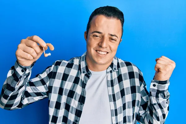 Elinde tıbbi işitme cihazı olan yakışıklı genç adam gururla bağırıyor, zaferi ve başarıyı kutluyor. 