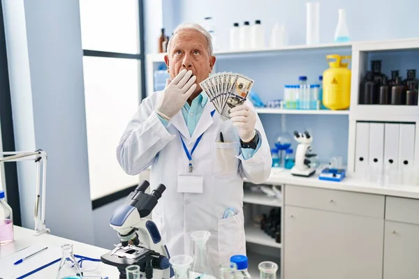 手で口を覆い 衝撃を与え 間違いを恐れているドルを保持している研究室で灰色の髪を持つ上級科学者 驚きの表情 — ストック写真