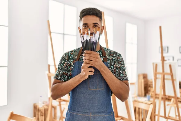 Genç Afrikalı Amerikalı sanatçı, resim stüdyosundaki fırçalarla ağzını kapayarak mutlu bir şekilde gülümsüyor..