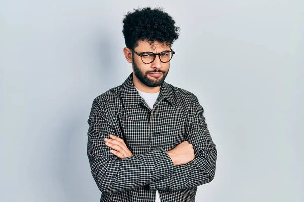 Sakallı, gözlüklü, kolları çapraz hareket eden, şüpheci ve gergin genç bir Arap, sorun yüzünden surat asıyor. negatif kişi. 