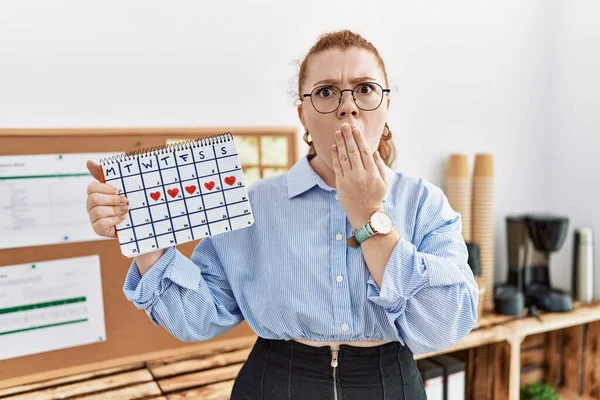 Mujer Pelirroja Joven Sosteniendo Calendario Del Corazón Oficina Cubriendo Boca — Foto de Stock