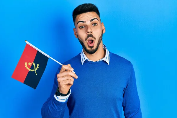 Young Hispanic Man Beard Holding Angola Flag Scared Amazed Open — Stockfoto