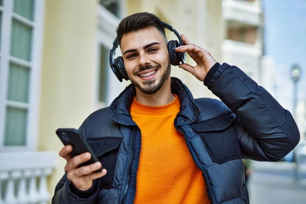 Yakışıklı, sakallı, neşeli, kendine güvenen, kışlık palto giyen, akıllı telefondan müzik dinleyen bir İspanyol.