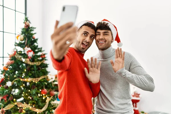 两只惊慌失措的男人在家里的圣诞树旁 用智能手机打着视频电话 — 图库照片