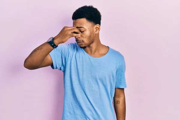 カジュアルブルーのTシャツを着た若いアフリカ系アメリカ人男性は 鼻をこすり 目は疲労と頭痛を感じます ストレスとフラストレーションの概念 — ストック写真