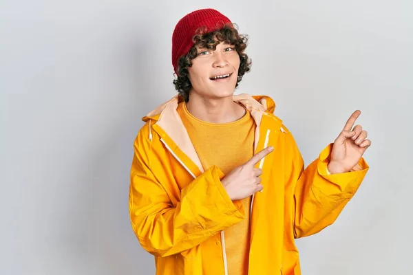 Joven Guapo Vistiendo Impermeable Amarillo Sonriendo Mirando Cámara Apuntando Con —  Fotos de Stock