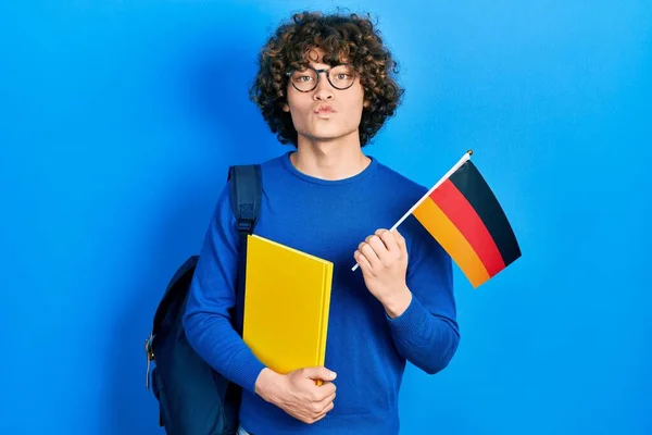 Guapo Joven Estudiante Intercambio Sosteniendo Bandera Alemania Mirando Cámara Soplando —  Fotos de Stock