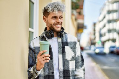 Genç İspanyol adam şehirde kahve içerken kulaklık takıyor..