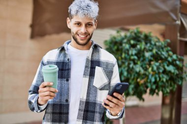 Genç İspanyol adam şehirde akıllı telefon kullanarak mutlu gülümsüyor..