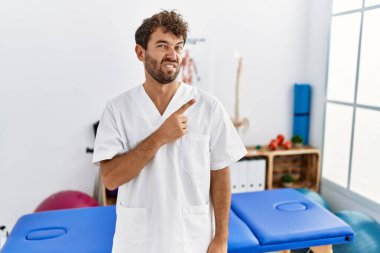 Ağrı kesici kliniğinde çalışan genç ve yakışıklı fizyoterapist endişeli ve endişeli bir ifadeye işaret ediyor. 