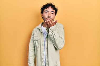 Gündelik giysiler giymiş genç İspanyol bir adam kameraya bakıp havada bir öpücük savuruyor ve sevimli ve seksi oluyor. aşk ifadesi. 