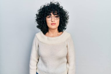 Orta Doğulu genç bir kadın günlük beyaz tişört giyiyor. Yüzünde ciddi bir ifade var. Basit ve doğal bir şekilde kameraya bakıyorsun.. 