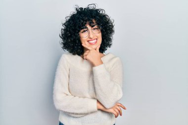 Orta Doğulu genç bir kadın günlük beyaz tişört giyiyor kameraya kendinden emin bakıyor kollarını kavuşturmuş ve çenesini kaldırmış gülümsüyor. Olumlu düşünmek. 