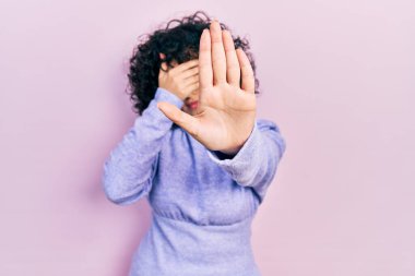 Orta Doğulu genç bir kadın, günlük kıyafetler giyiyor, elleriyle gözleri örtüyor ve üzgün ve korku ifadeleriyle jest yapıyor. utangaç ve olumsuz kavram. 