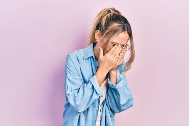 Güzel, genç, sarışın bir kadın gündelik kıyafetler giyiyor ve ağlarken suratını ellerle kapatan üzgün bir ifade takınıyor. depresyon kavramı. 