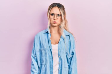 Gündelik kıyafetler giyen, gözlüklü, komik yüzlü güzel sarışın kadın. Havayla şişmiş ağız, çılgın bir ifade.. 