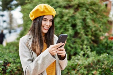 Genç İspanyol kız şehirde akıllı telefon kullanarak mutlu bir şekilde gülümsüyor..