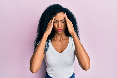 Orta yaşlı Afro-Amerikalı kadın, günlük beyaz tişört giyiyordu. Elleri başının üstünde, stres yüzünden baş ağrısı vardı. migren ağrısı. 