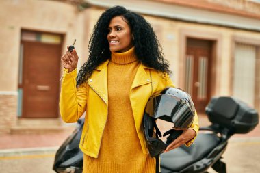 Orta yaşlı Afro-Amerikalı kadın şehirde motosiklet anahtarı ve miğferi tutuyor..