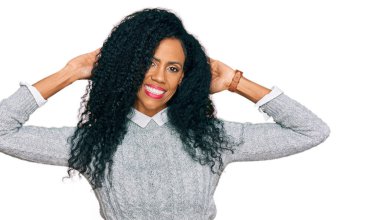 Orta yaşlı Afro-Amerikalı kadın günlük kıyafetler giyiyor, rahatlıyor ve esniyor, kolları ve elleri başının arkasında ve boynunun arkasında mutlu bir şekilde gülümsüyor. 