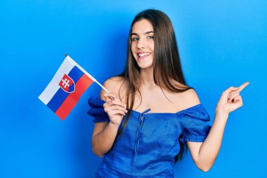 Slovakya bayrağı tutan genç esmer kız mutlu bir şekilde gülümsüyor. 