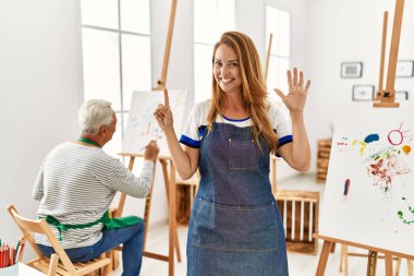 Resim stüdyosunda önlük giyen İspanyol kadın altı numarayı gösterip işaret ederken kendine güvenen ve mutlu bir şekilde gülümsüyor.. 