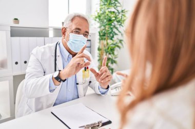 Orta yaşlı erkek ve kadın doktor ve hasta tıbbi maske takıyor klinikte danışmanlık yapıyorlar.
