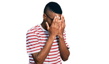 Genç Afro-Amerikalı bir adam günlük tişört giyiyor ve ağlarken yüzünü ellerle kapatan üzgün bir ifade takınıyor. depresyon kavramı. 