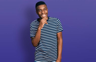 Sıradan çizgili tişört giyen genç bir Afro-Amerikan erkeği kameraya kollarını kavuşturup çenesini kapatarak gülümsüyor. Olumlu düşünmek. 