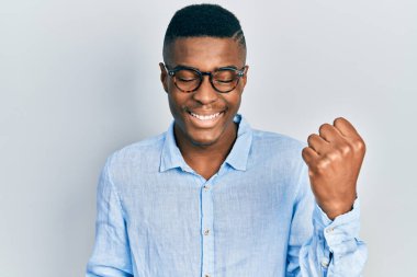 Sıradan kıyafetler ve gözlük takan genç Afrikalı Amerikalı adam başarıyı kolları havada ve gözleri kapalı kutluyor ve şaşırıyor. 