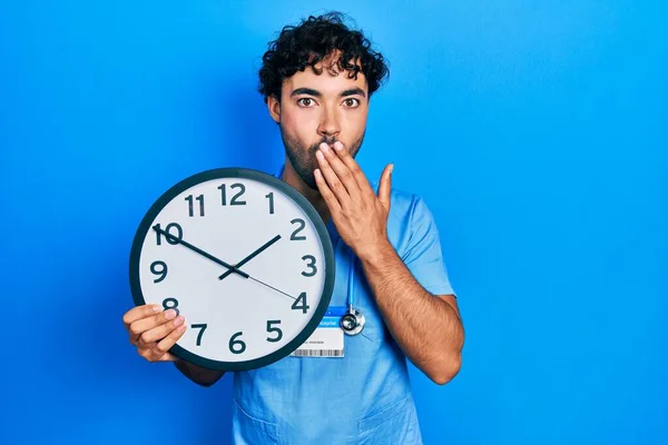 Joven Hispano Vestido Con Uniforme Enfermero Azul Sosteniendo Reloj Cubriendo — Foto de Stock