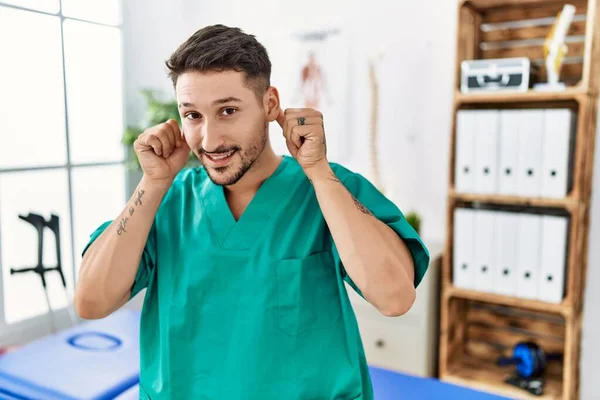 Ağrı Kesici Kliniğinde Çalışan Genç Bir Fizyoterapist Gülümsüyor Kulaklarını Parmaklarıyla — Stok fotoğraf