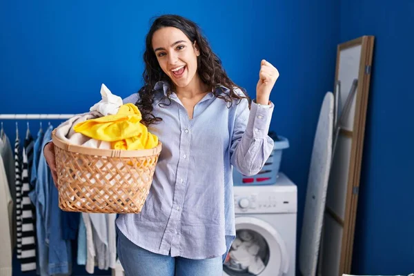 Çamaşır sepetini tutan genç esmer kadın gururla bağırıyor zaferi kutluyor ve başarıyı kollarını kaldırarak kutluyor. 