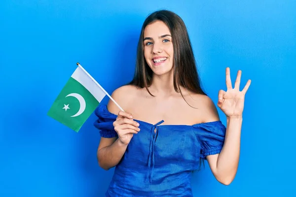 Young Brunette Teenager Holding Pakistan Flag Doing Sign Fingers Smiling — стоковое фото
