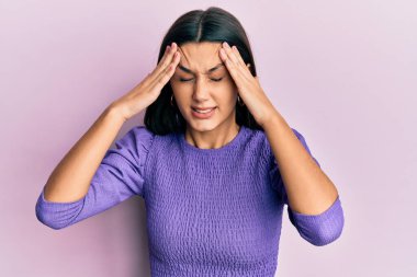 Elleri başının üstünde, günlük kıyafetler giyen genç İspanyol kadın, stres yüzünden baş ağrısı çekiyor. migren ağrısı. 