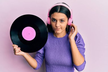 Latin kökenli genç bir kadın, elinde vinil disk tutan, kuşkucu ve gergin kulaklık takıyor, sorun yüzünden kaşlarını çatıyor. negatif kişi. 