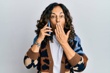 Orta yaşlı İspanyol bir kadın akıllı telefonla konuşuyor ağzını eliyle kapatıyor, şok geçiriyor ve hata yapmaktan korkuyor. şaşırmış ifade 